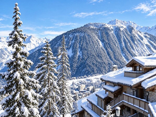 A snow-covered mountain landscape with a wooden chalet-style building featuring balconies and a stone facade.