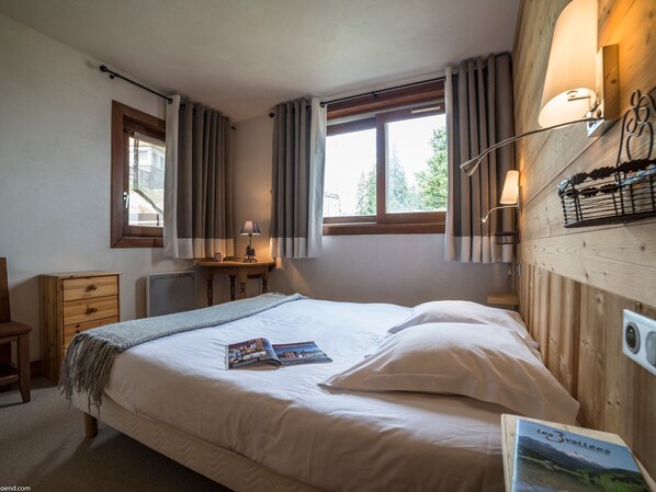 A bedroom with a bed, a nightstand, a lamp, and a window with curtains.