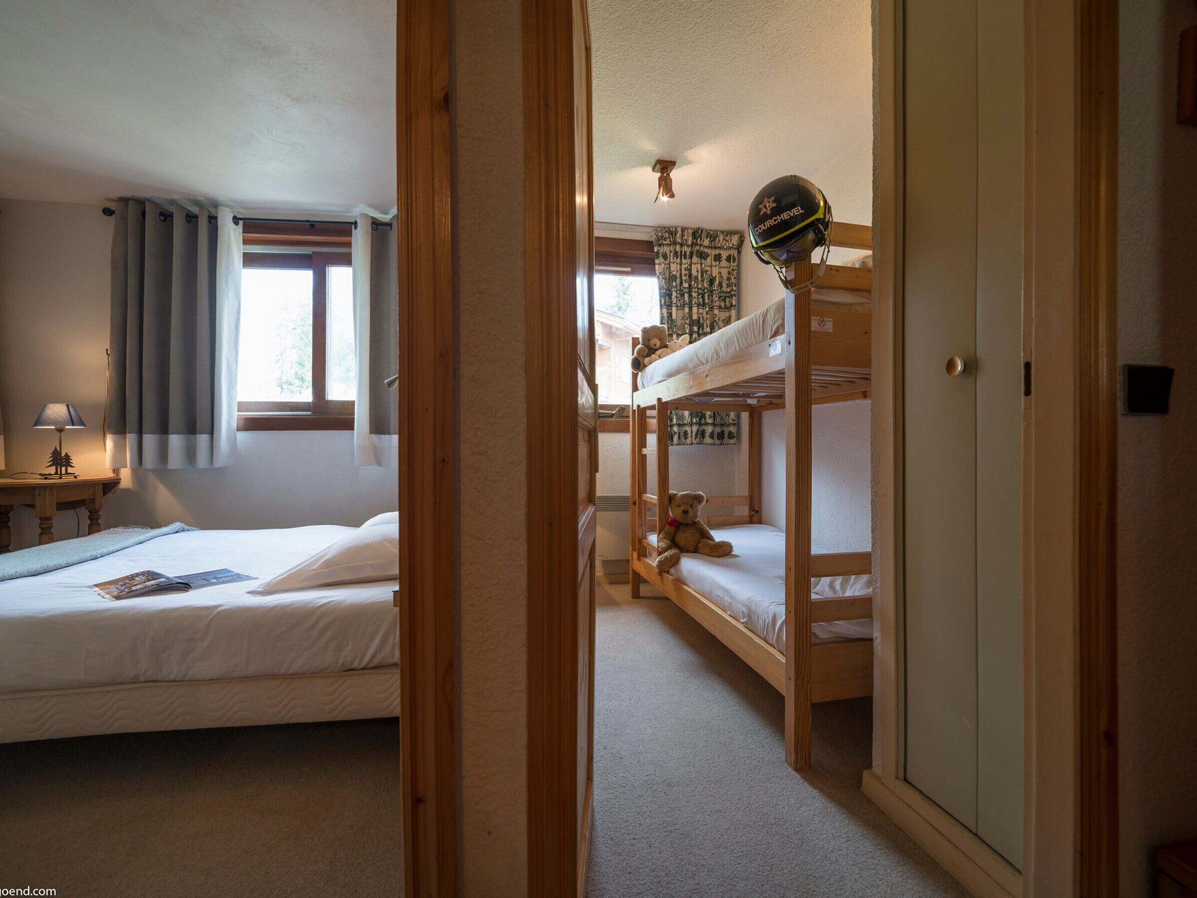 A room with two bunk beds, a desk with a lamp, and a window with curtains.