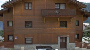 Ein mehrstöckiges Holzgebäude mit Balkon, einem Schild mit der Aufschrift 'HOME Courchevel' und einem geparkten Auto davor.