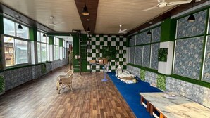 A spacious room with a wooden floor, a long table, and a blue carpeted area. - Namoh Stay (Rishikesh)