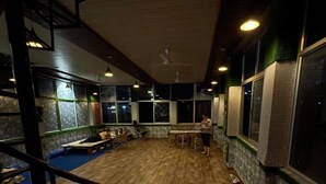 A spacious room with a wooden floor, large windows, and a seating area with tables and chairs. - Namoh Stay (Rishikesh)