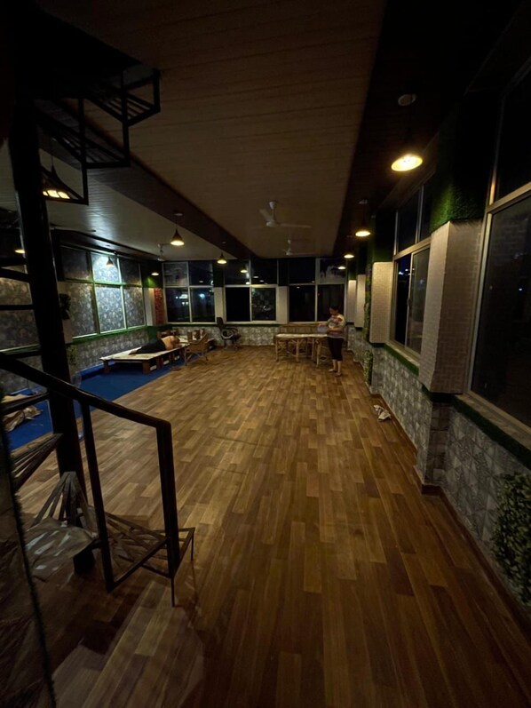 A spacious room with a wooden floor, large windows, and a seating area with tables and chairs. - Namoh Stay (Rishikesh)