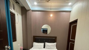 A neatly made bed in a hotel room with a ceiling fan, a bedside table, and a mirror on the wall. - Namoh Stay (Rishikesh)