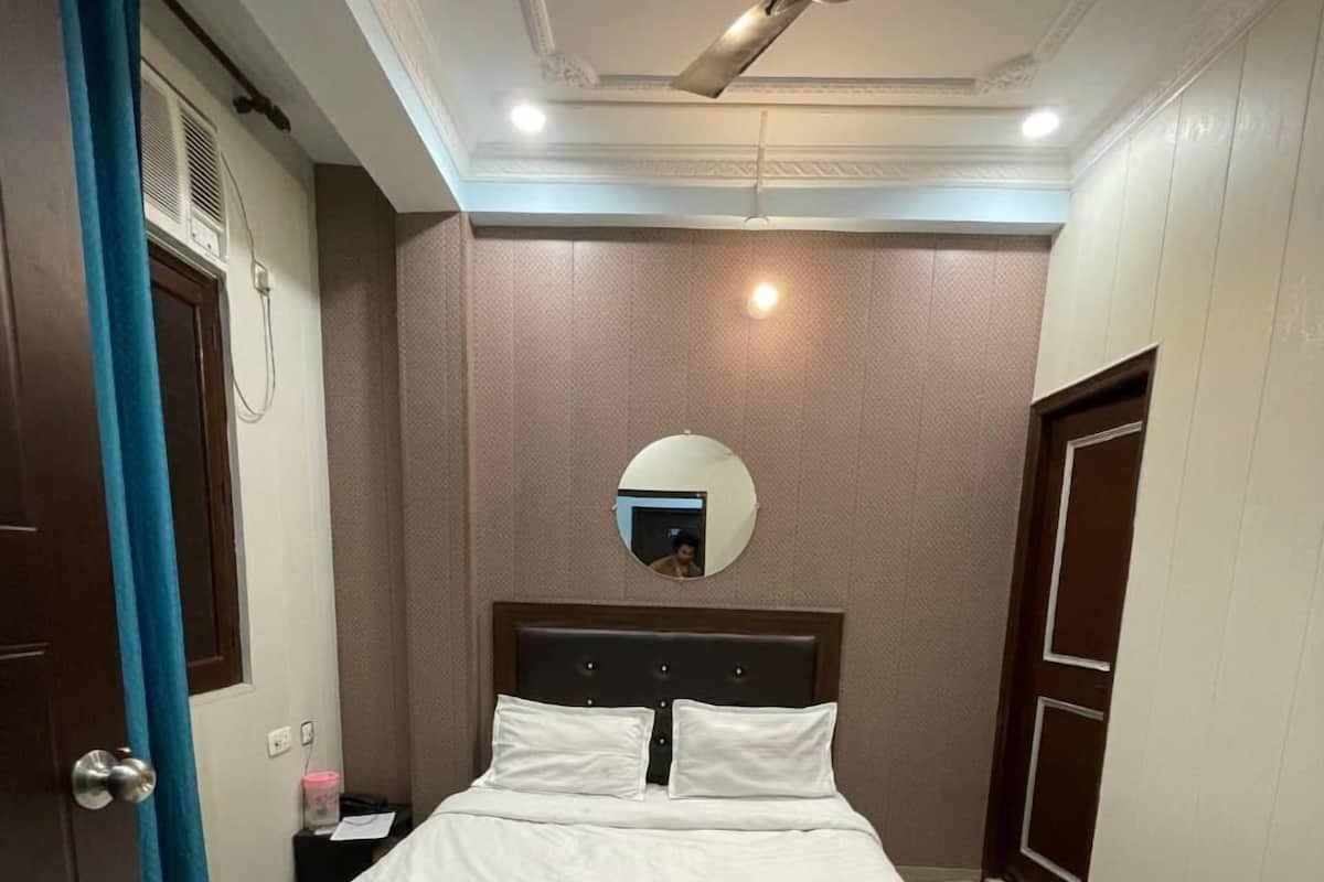 A neatly made bed in a hotel room with a ceiling fan, a bedside table, and a mirror on the wall.