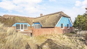 A traditional thatched-roof house with blue wooden walls and a brick foundation.
