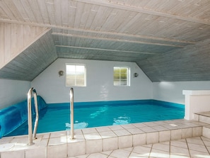 An indoor swimming pool with a sloped ceiling and two windows.