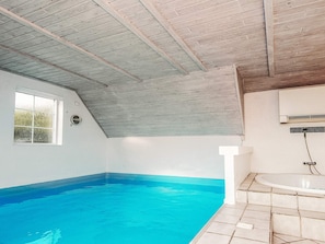 A swimming pool with a tiled edge, a window, and a ceiling with wooden beams.