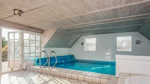 An indoor swimming pool with a blue jacuzzi, tiled flooring, and wooden ceiling beams.