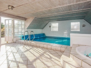 An indoor swimming pool with a blue jacuzzi, tiled flooring, and wooden ceiling beams.