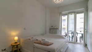 A bedroom with a bed, a bedside lamp, a small stool, and a view of the outside balcony. - Turati Family Apartment (Lecco)