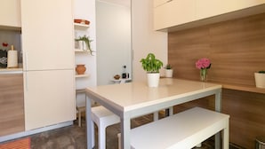 A modern kitchen with white cabinetry, a white countertop, and a bench. There are potted plants on the countertop and a wooden wall in the background. - Turati Family Apartment (Lecco)