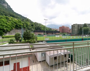 A sports field with a netted fence, surrounded by buildings and trees. - Turati Family Apartment (Lecco)