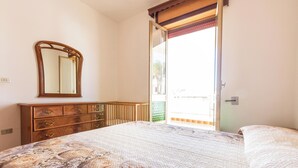 Une chambre à coucher comprenant un lit, une commode, un miroir et une porte donnant sur un espace extérieur.