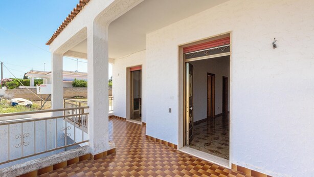 Un couloir doté d’un sol à carreaux, de murs blancs et d’un balcon avec une balustrade.
