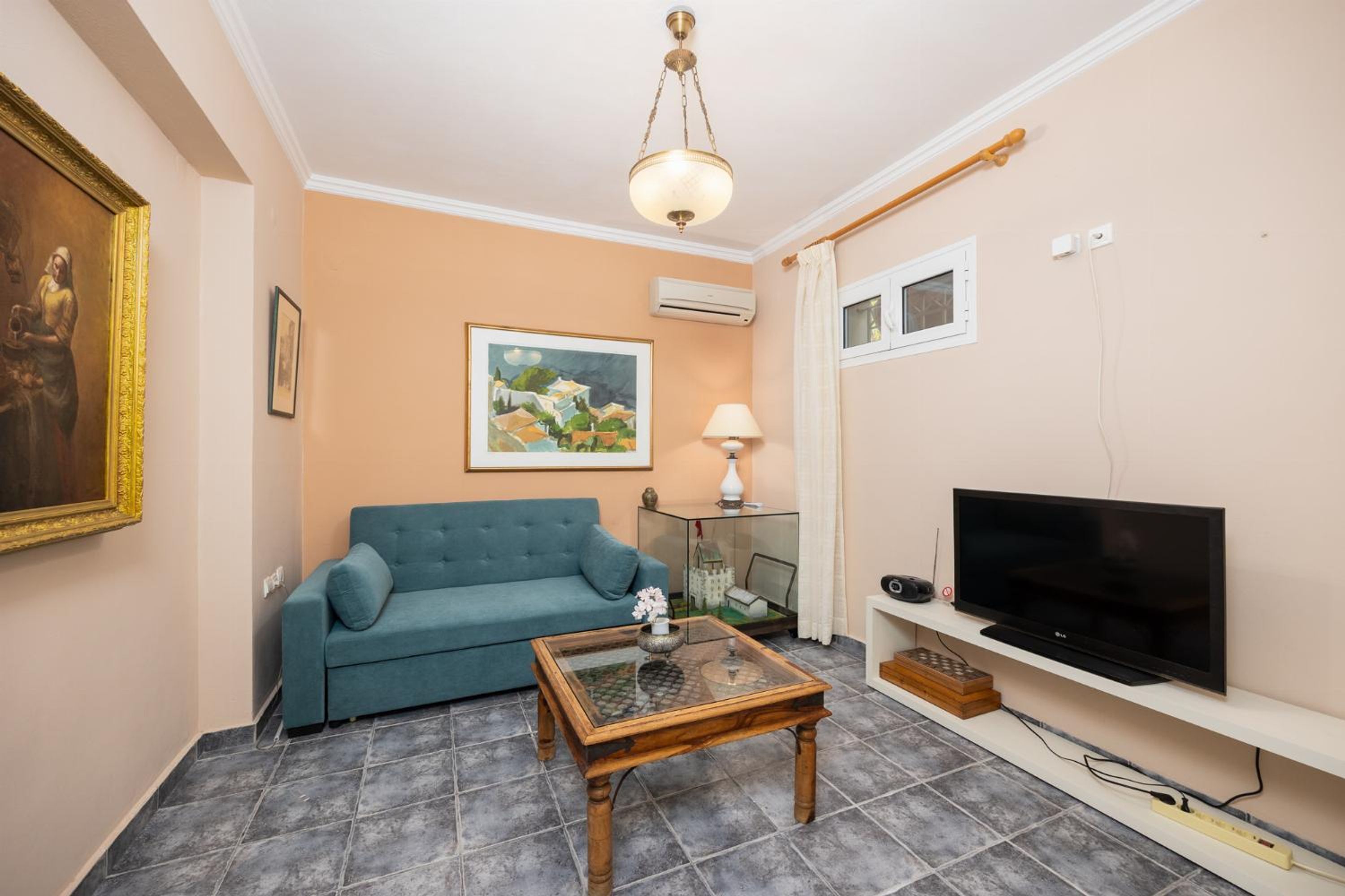 A living room with a teal sofa, a glass coffee table, a flat-screen TV, and a painting on the wall.