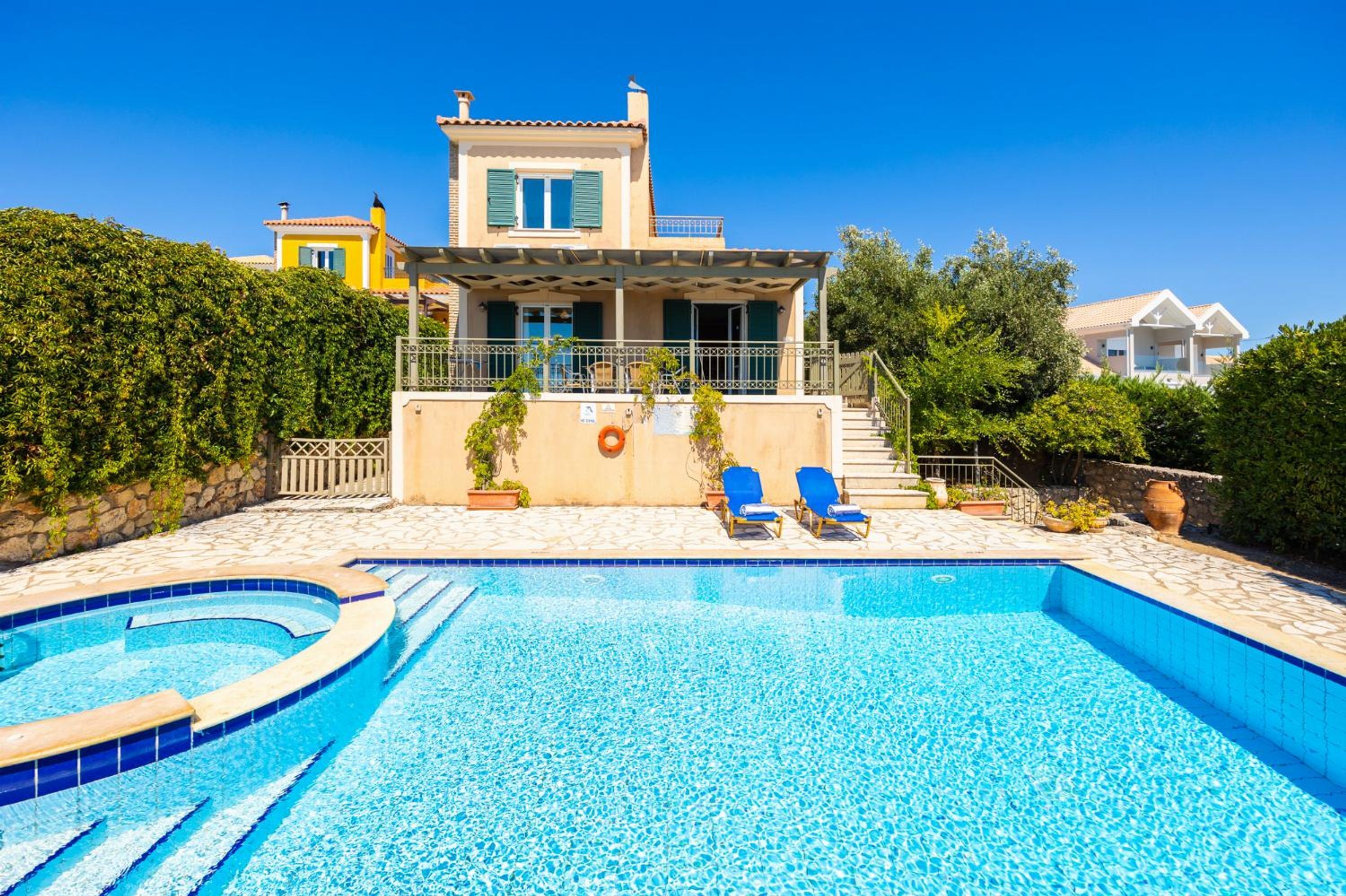 A swimming pool with two lounge chairs, a covered patio, and a two-story house with a balcony.
