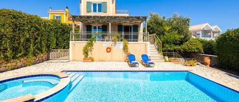 A swimming pool with two lounge chairs, a covered patio, and a two-story house with a balcony.