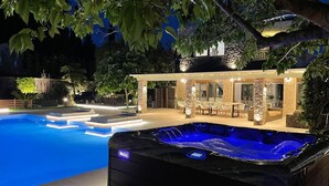 Een zwembad met een hottub op de voorgrond, een overdekt terras en een huis in de verte.