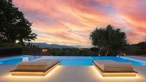 A pool area with two lounge chairs and a view of the mountains at sunset.