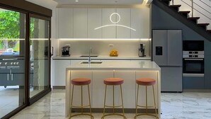 Een moderne keuken met een marmeren aanrecht, drie krukken, een koffieapparaat en een inbouwoven.