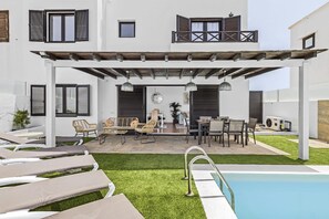 Ein zweistöckiges Gebäude mit überdachter Terrasse, Sitzgelegenheiten im Freien und einem Swimmingpool.