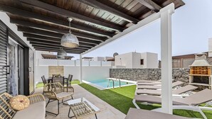 Un patio exterior con mobiliario de mimbre, una piscina y un muro de piedra.