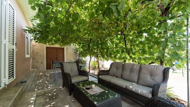 An outdoor seating area with wicker furniture, a stone-tiled floor, and a view of a building with a stone facade and a door.