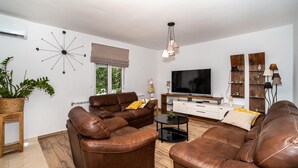 A modern living room with leather sofas, a flat-screen TV, wooden flooring, and a decorative wall clock.