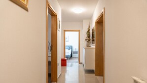 A narrow hallway with wooden doors and a tiled floor leading to a bedroom area with a bed and nightstands.
