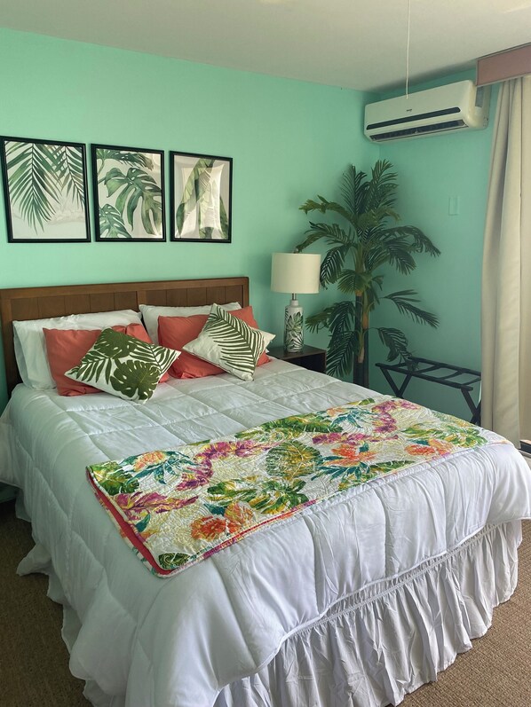 A neatly made bed with a floral quilt, a wooden headboard, and a nightstand with a lamp. - Charming beach front condo, Freeport ,Coral Beach, with AC/WiFi, salon/spa, pool (Freeport)