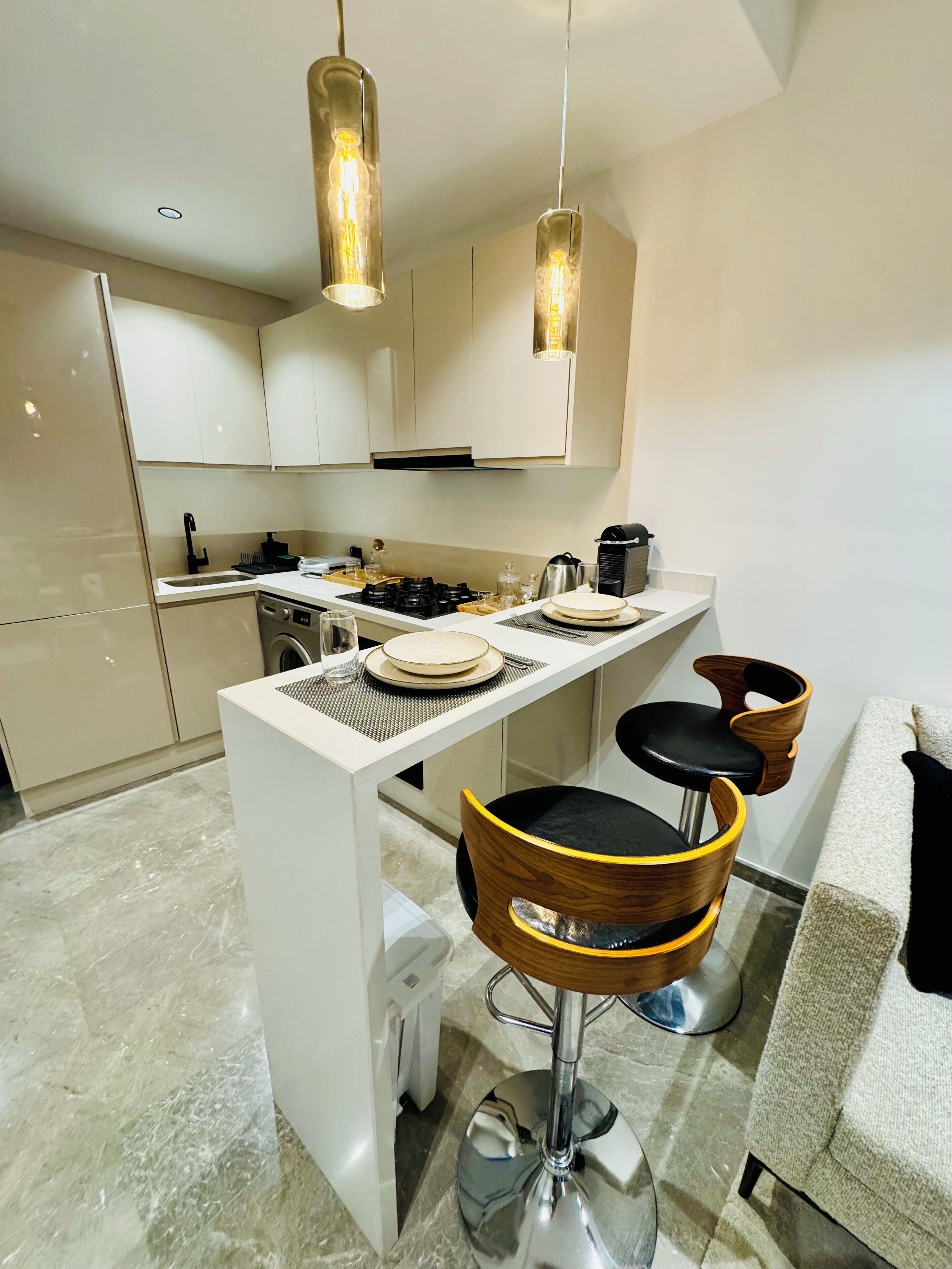Une cuisine moderne avec des meubles blancs, un îlot central doté de tabourets et un éclairage suspendu.