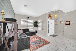 Una sala de estar moderna con un sofá gris, un tapete estampado y una escalera que conduce a otro nivel.