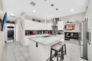 A modern kitchen with a large island, white cabinetry, and a black leather sofa in the adjacent living area.