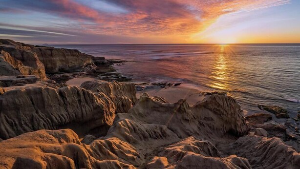 A coastal landscape with rocky formations and a sunset over the ocean.