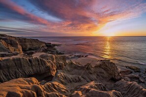 A coastal landscape with rocky formations and a sunset over the ocean.