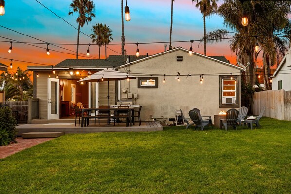 A backyard with a patio area, outdoor seating, and string lights.