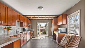 A modern kitchen with wooden cabinets, a marble countertop, and a view to the outside.