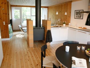 A modern kitchen with a wood stove, white cabinets, and a dining area with a round table and chairs. - 6 Person Holiday Home in Vaeggerlose (Vaeggerlose)