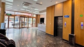 Un vestíbulo de hotel con mostrador de recepción, puerta de vidrio de acceso y un panel informativo digital.