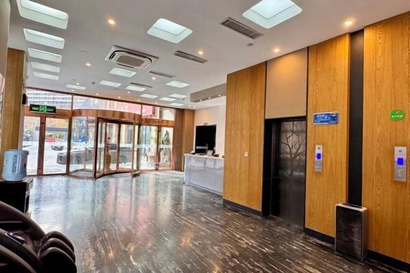 A hotel lobby with a reception desk, a glass door entrance, and a digital information board.