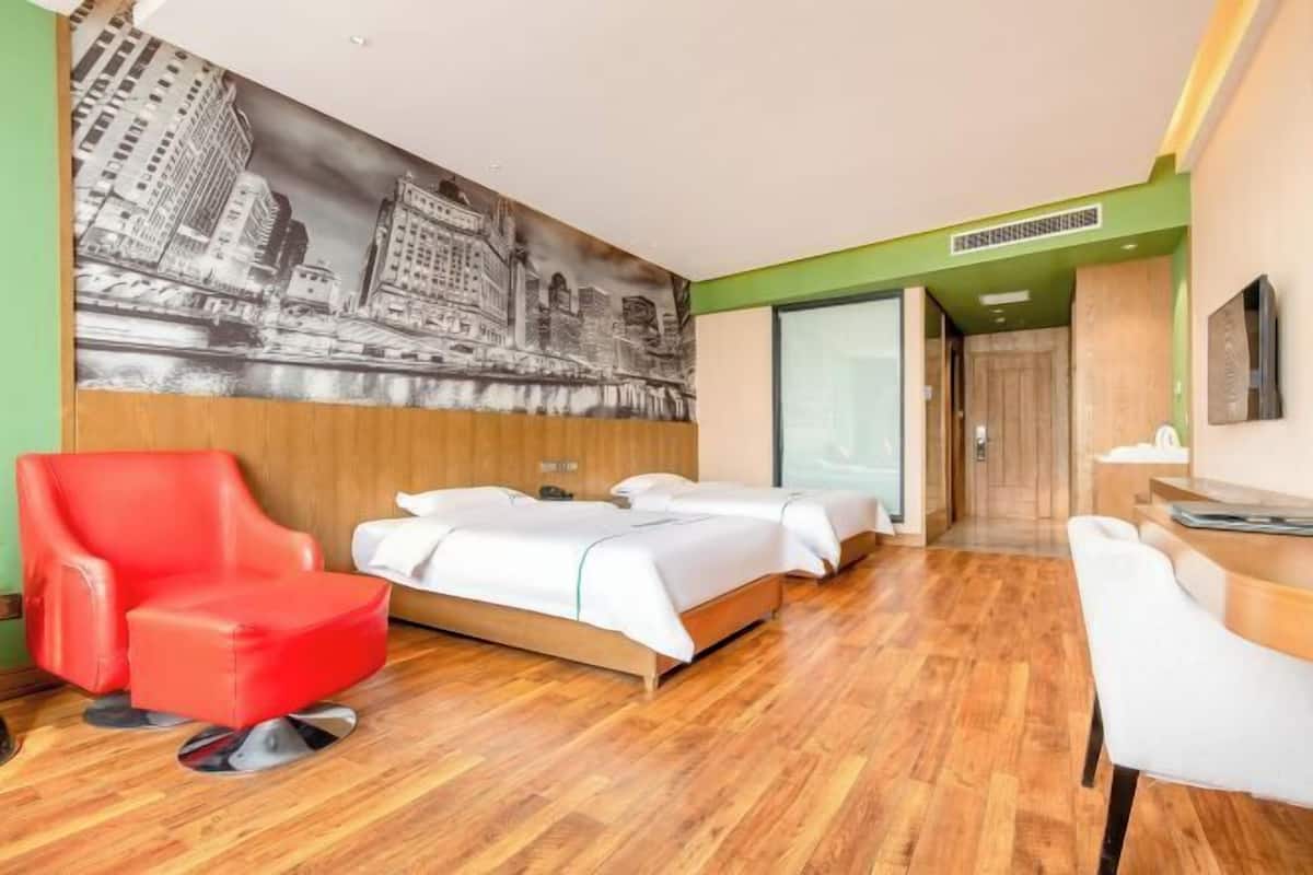 A hotel room with a large bed, a red armchair, a white desk, and a cityscape mural on the wall.