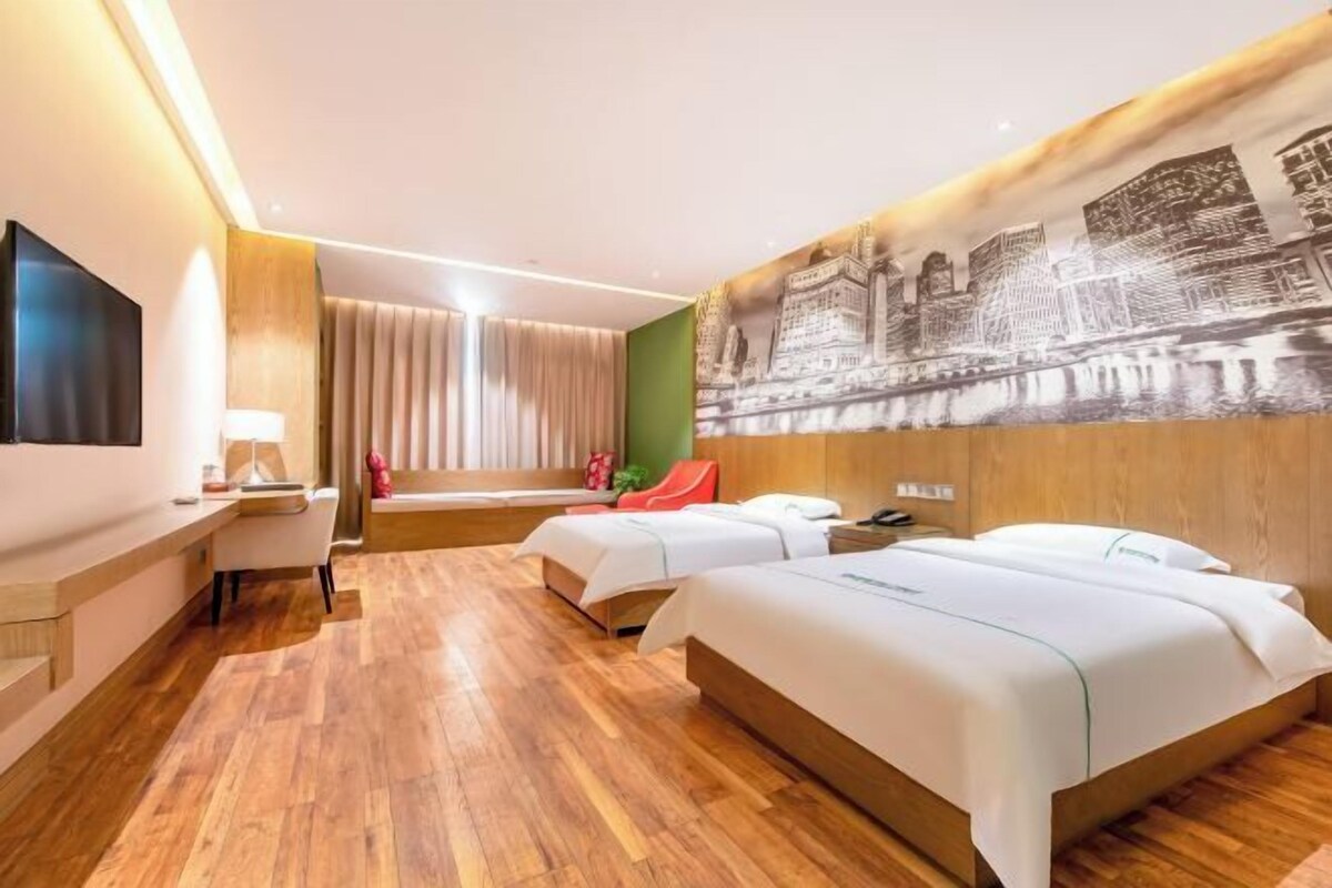 A hotel room with two beds, a flat-screen TV, a desk, and a large cityscape mural on the wall.