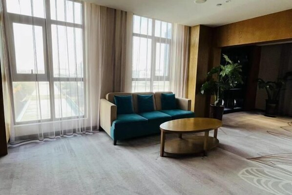 A modern living room with a sofa, a coffee table, and large windows with sheer curtains. - Xiyue Hotel (Zhengzhou east station store) (Zhengzhou)