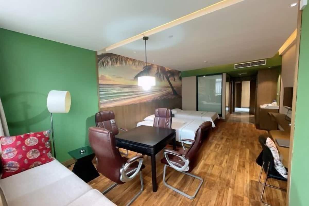A hotel room with a bed, two single beds, a dining table with chairs, a sofa, a lamp, and a mural on the wall.