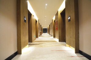 Un couloir d’hôtel avec un sol recouvert de moquette, des murs en bois et des panneaux lumineux fixés aux murs.