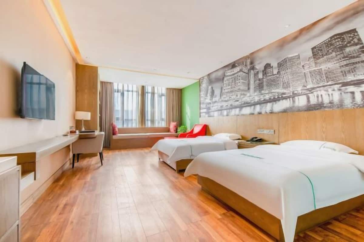 A hotel room with two beds, a desk, a chair, a TV, and a large cityscape mural on the wall.