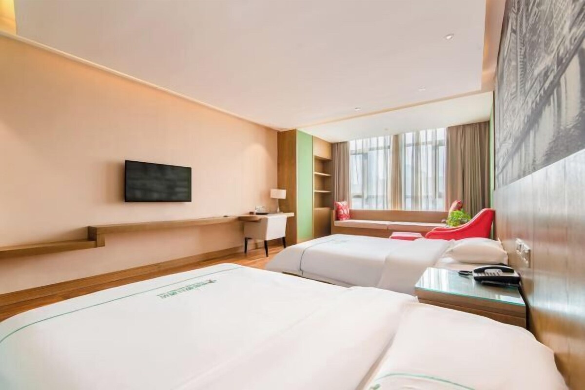 Une chambre d’hôtel avec deux lits, un bureau, une chaise, une télévision et une fenêtre avec des rideaux.
