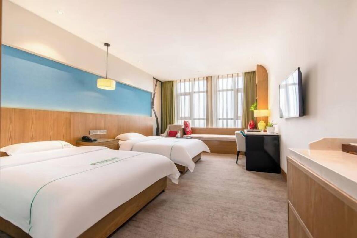 A hotel room with two beds, a desk, a TV, and a window with curtains.
