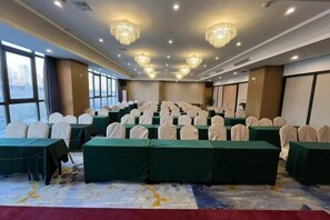 A conference room with rows of tables and chairs, large windows, and chandeliers.